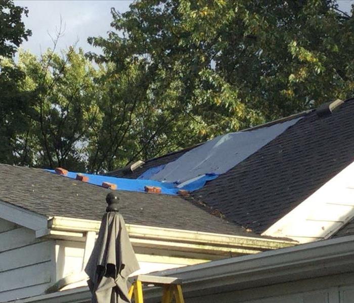 A blue tarp covers a portion of the roof of a residential home. 