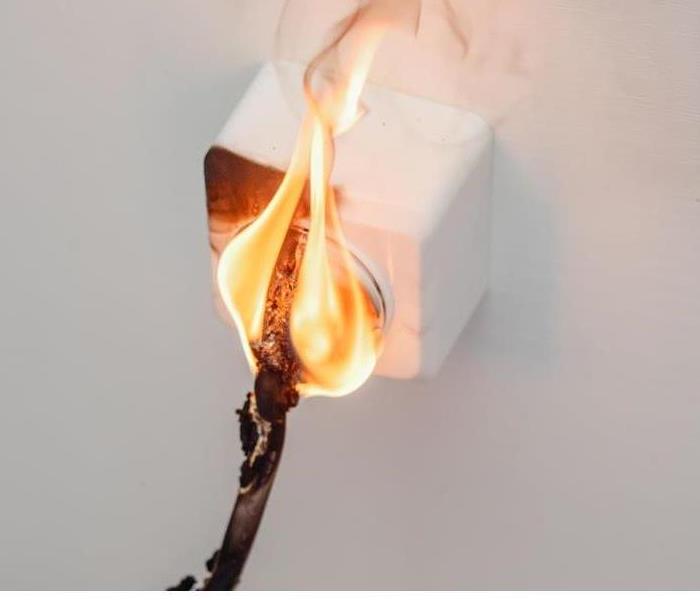 An electrical fire burns atop a cord that is plugged into an outlet 